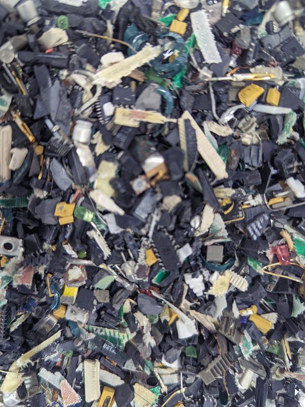 Shredded electronic scrap in close-up: thousands of fragments of circuit board, metal and plastic sorted to a uniform size.