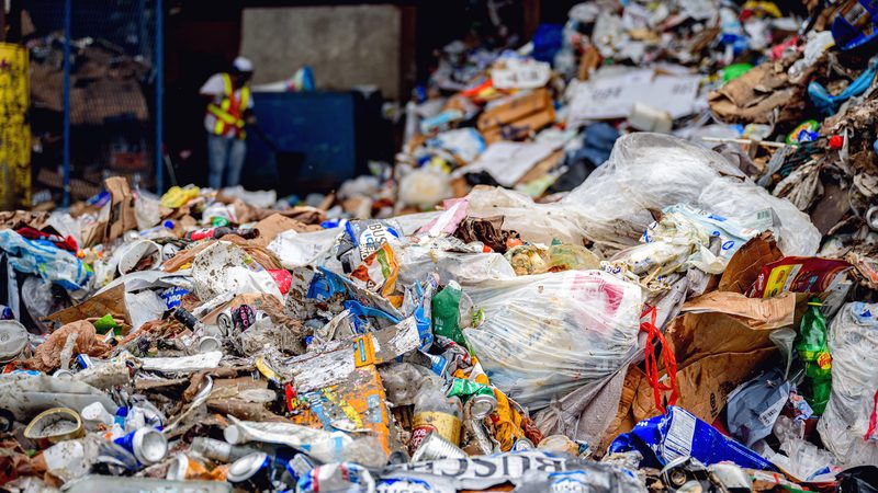The tipping floor of a municipal recycling facility: a mound of mixed recyclables under an open-sided shed.
