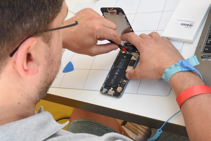 Close view of hands opening a mobile phone at a workbench, the battery and board exposed.