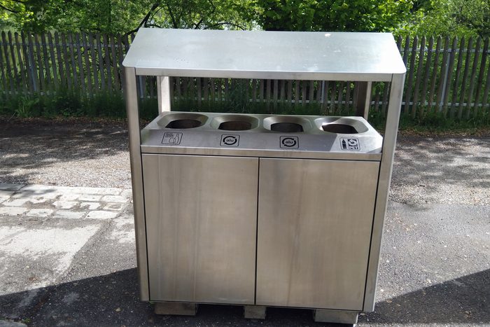 A four-stream stainless recycling station on a path, four labeled apertures across the top.