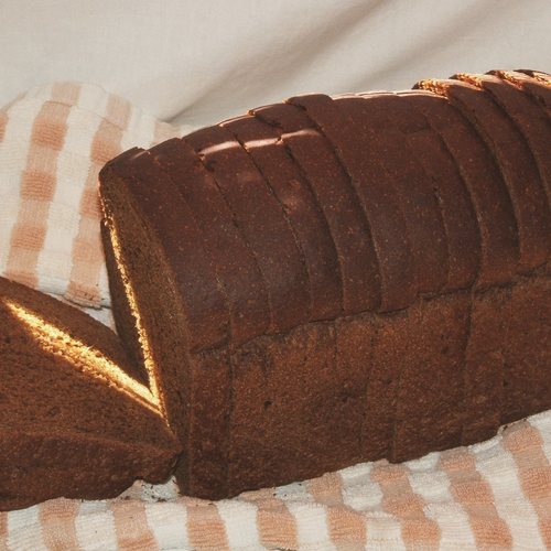 A sliced dark rye loaf on a chequered cloth.
