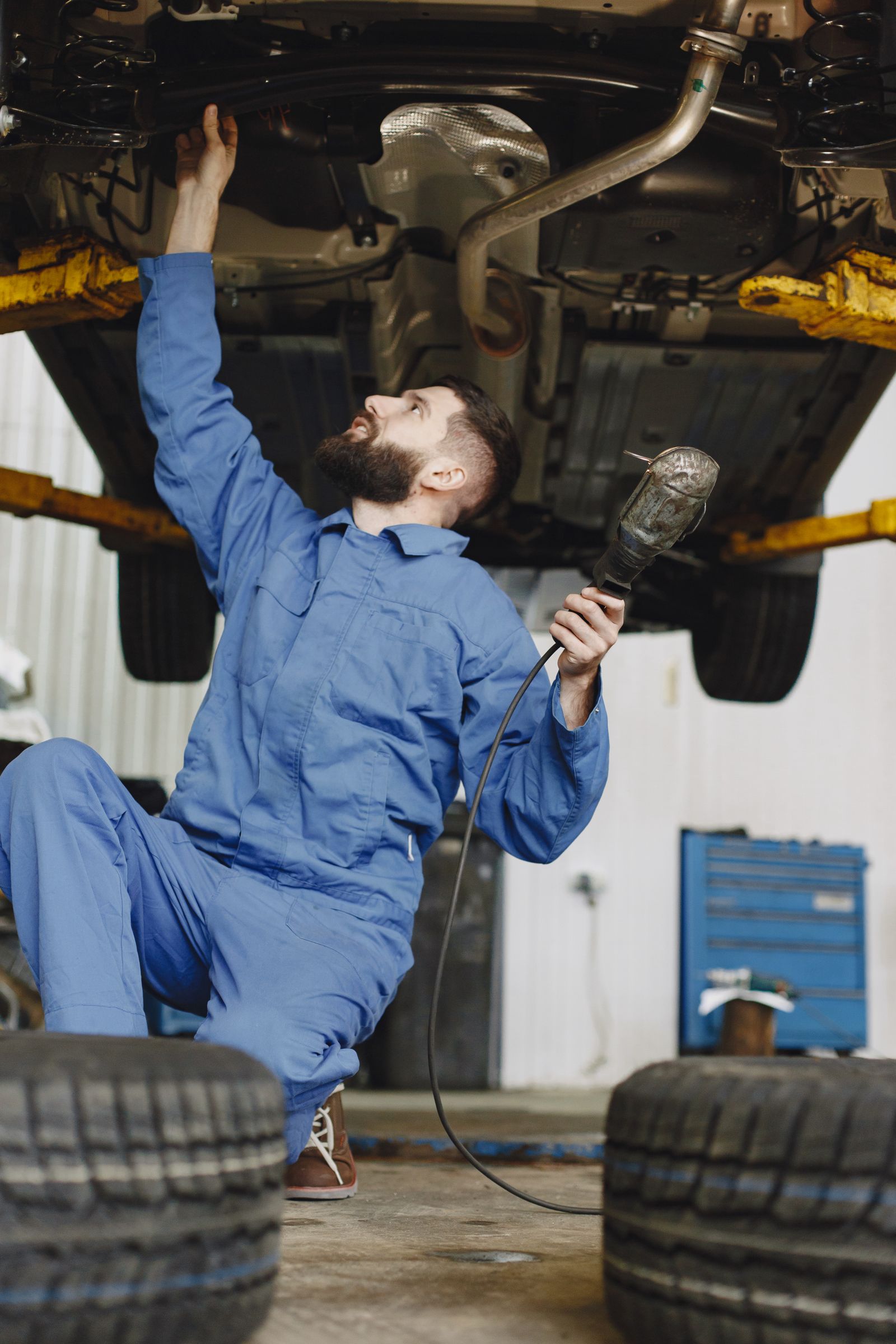 A technician working underneath a raised vehicle with a hand tool.