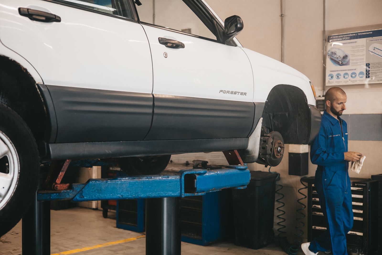 A pickup raised on a two-post lift with a technician working alongside it.
