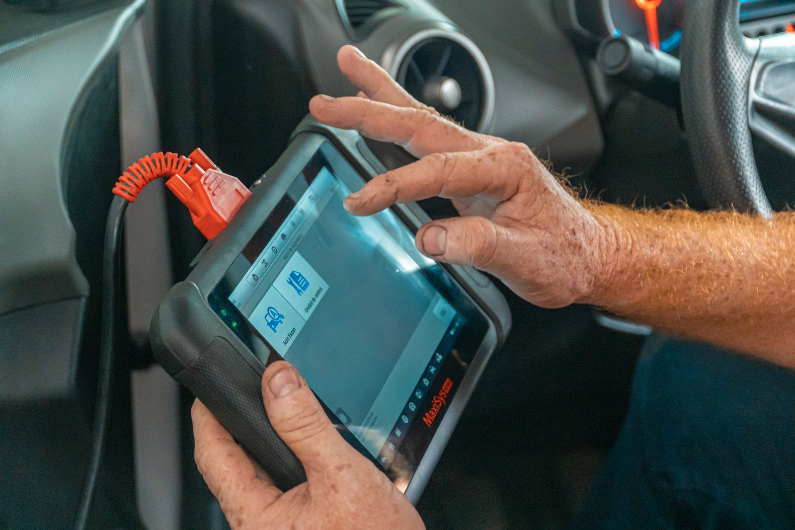 A technician holding a diagnostic scan tool connected inside a vehicle.