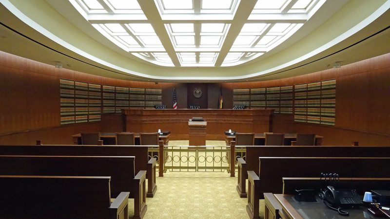 An empty American appellate courtroom: a long curved bench beneath a coffered skylight, counsel tables in front of it and a low rail across the room.