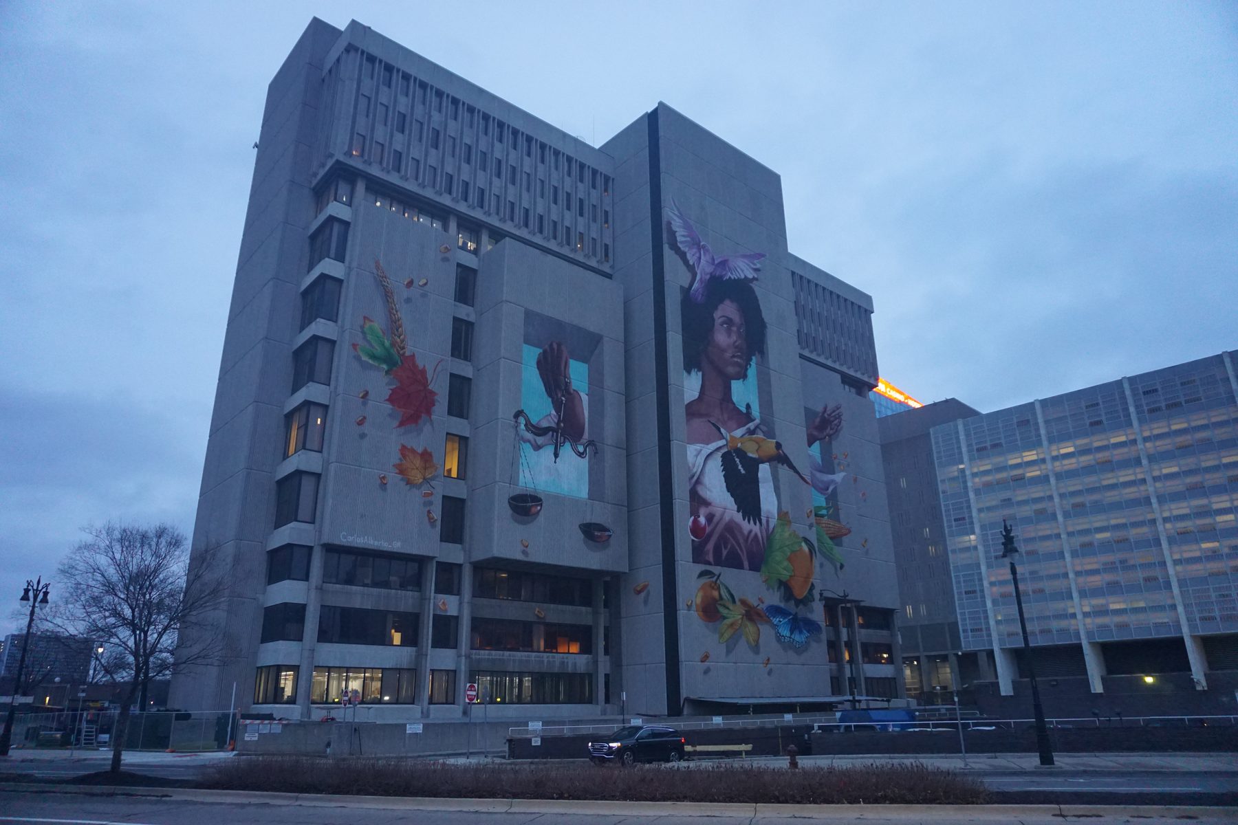 Frank Murphy Hall of Justice in Detroit at dusk — a concrete tower carrying a large painted mural, seen from the street.