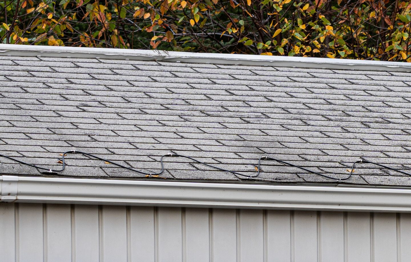 Asphalt shingles above a gutter, with a heat cable along the roof edge
