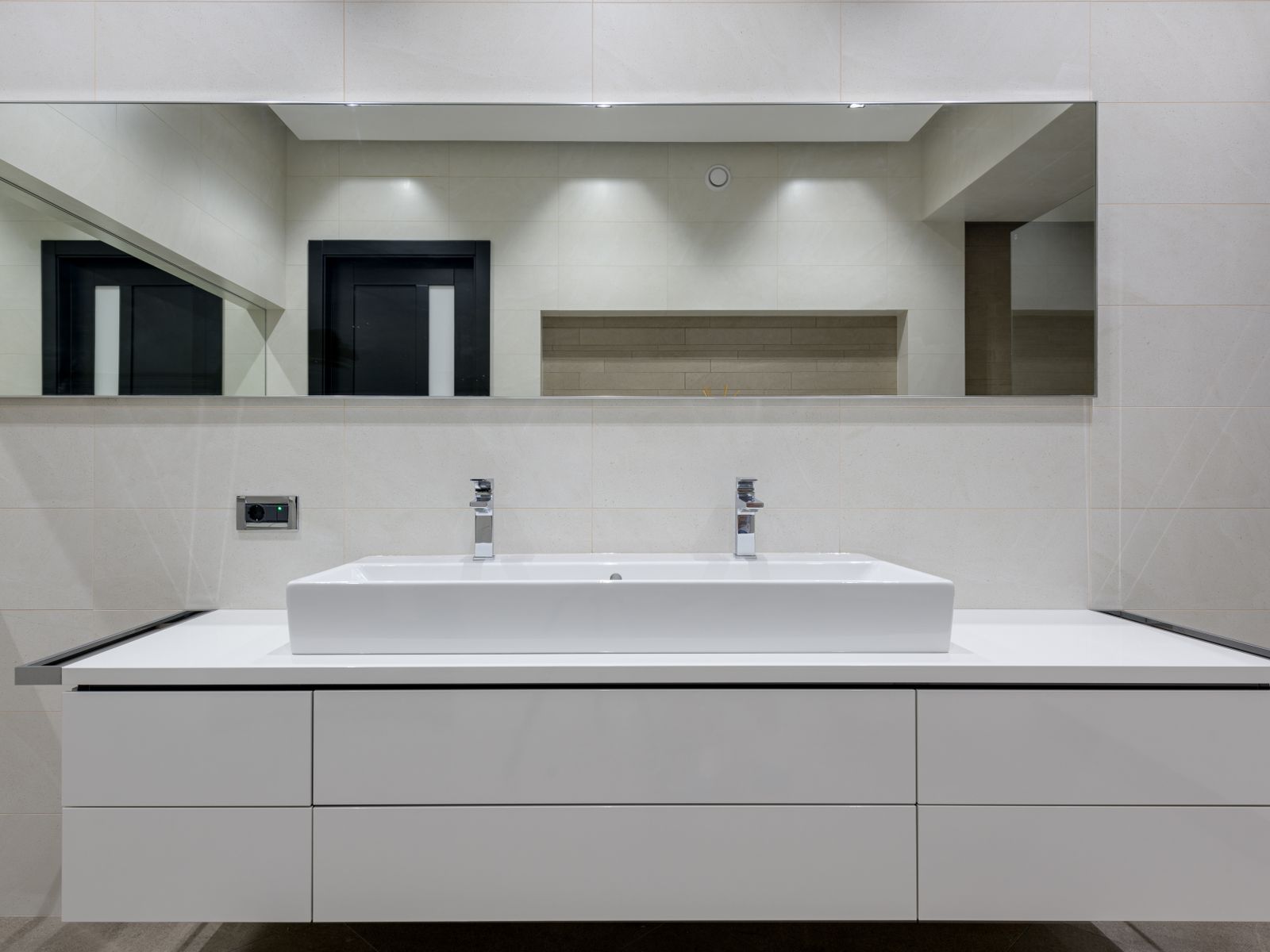 A finished primary bath vanity: one long basin, full-width mirror, stone-tiled wall.