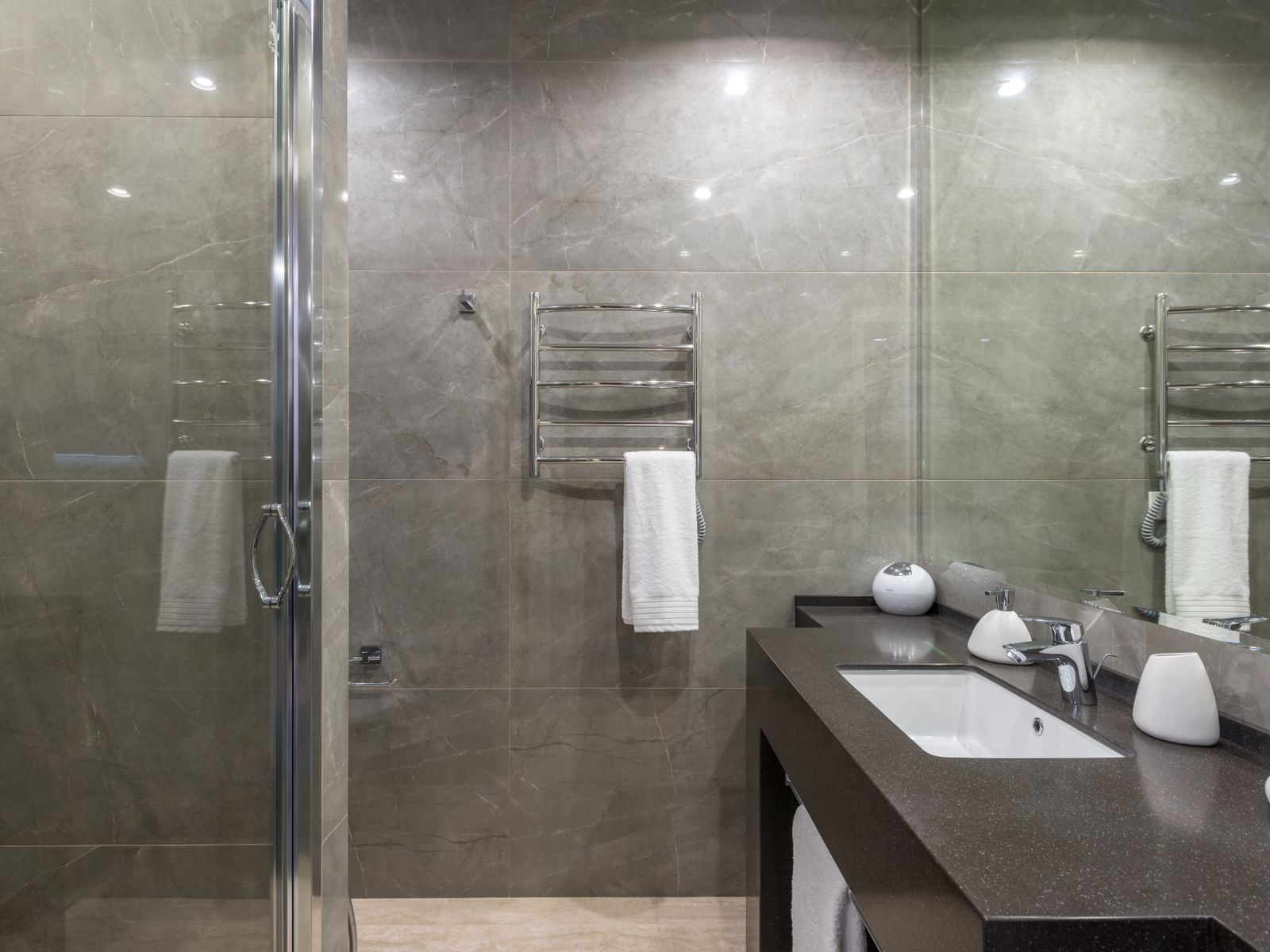 A finished bath in large-format stone tile, with a glassed shower and a dark stone vanity top.