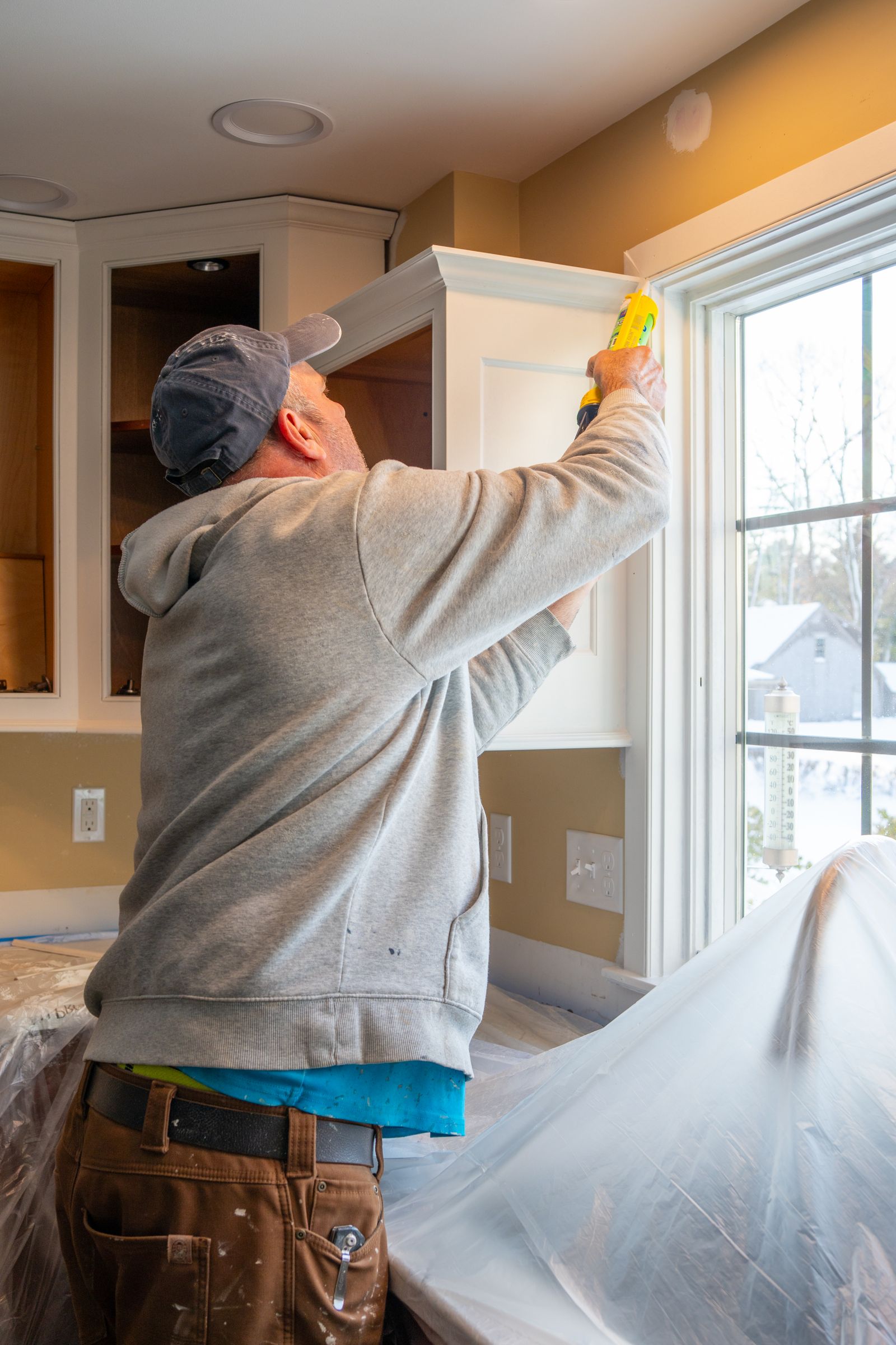 A carpenter fitting cabinetry against a wall.