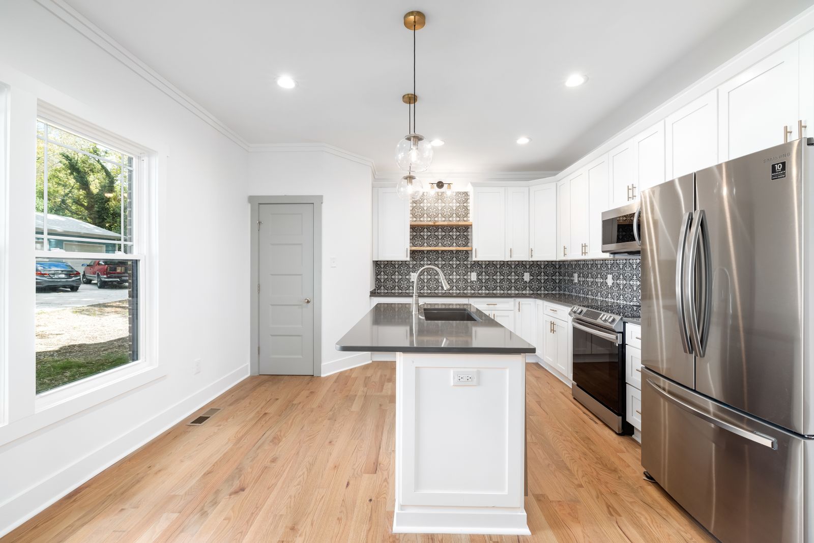 A bright white kitchen with a large island, pendant lighting and oak flooring.