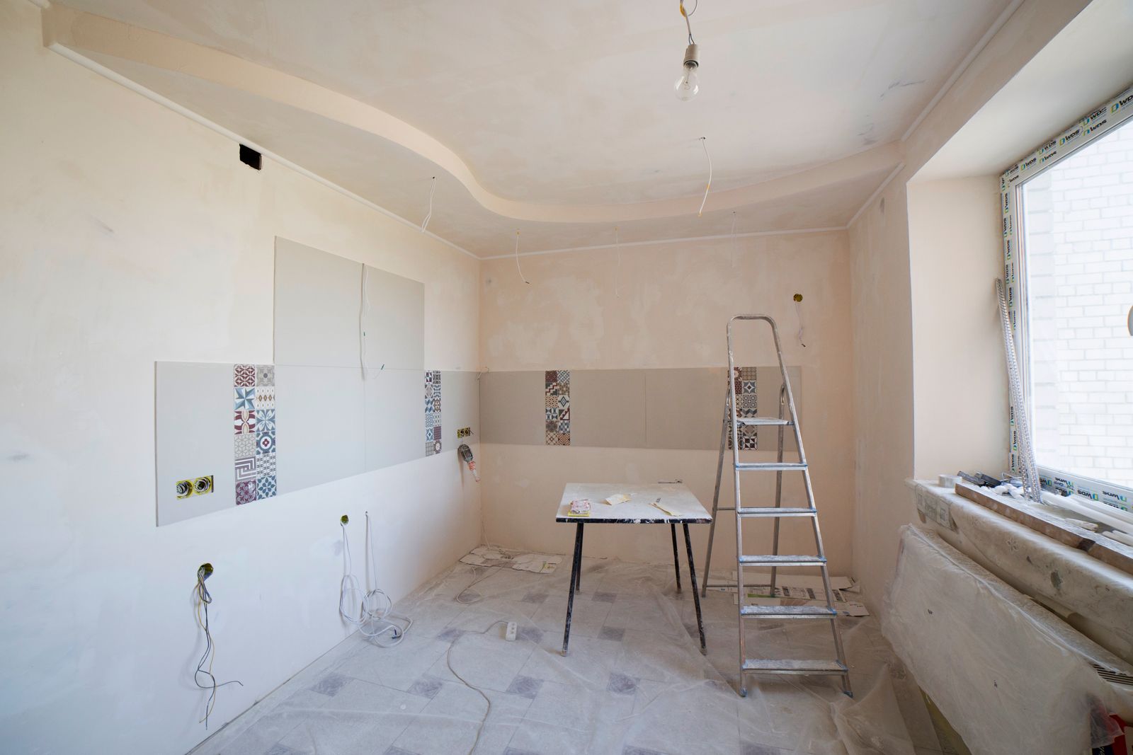 A room mid-renovation with protective sheeting on the floor and a ladder in place.