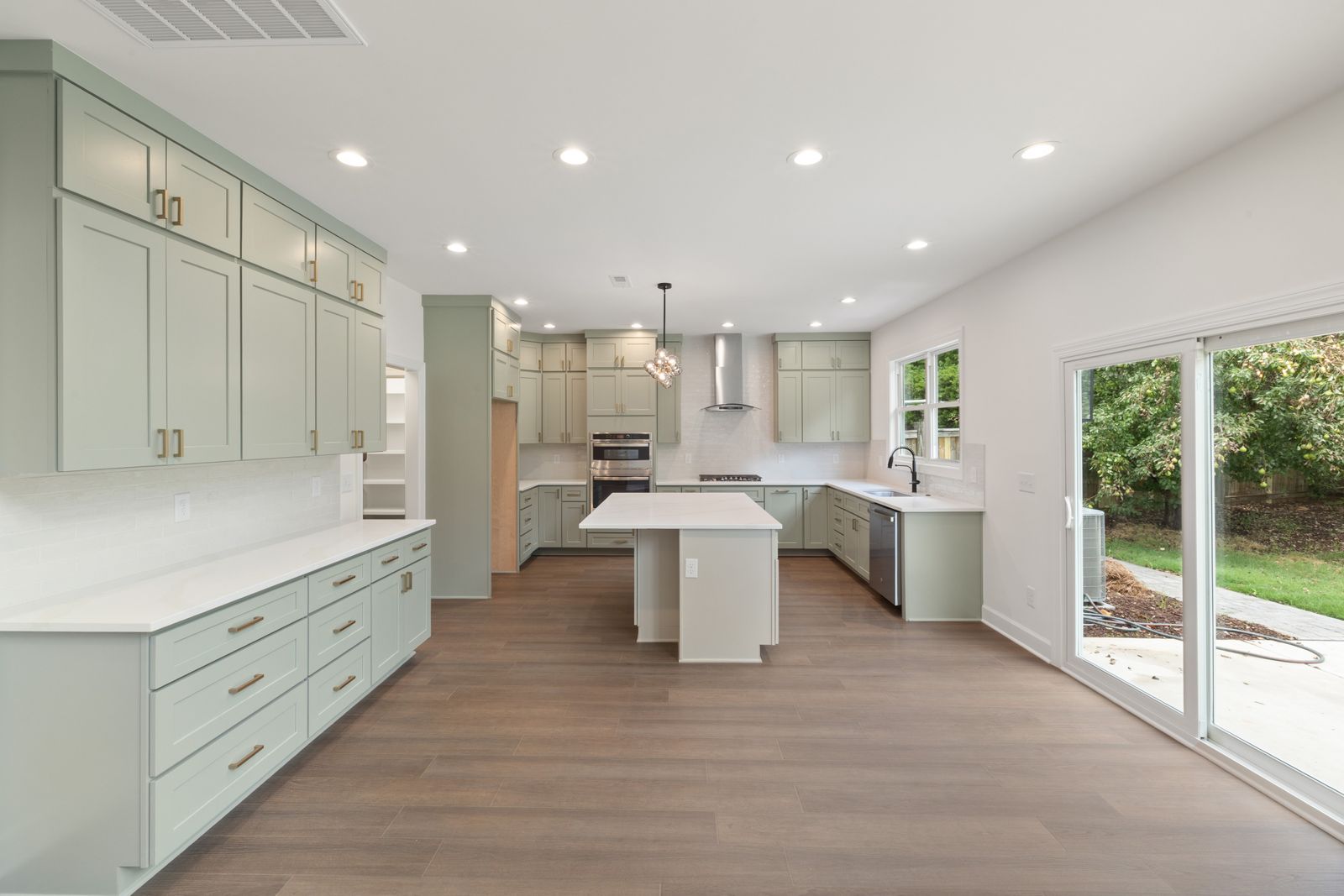 A finished kitchen with sage-green cabinetry, a long island, oak flooring and full-height windows.
