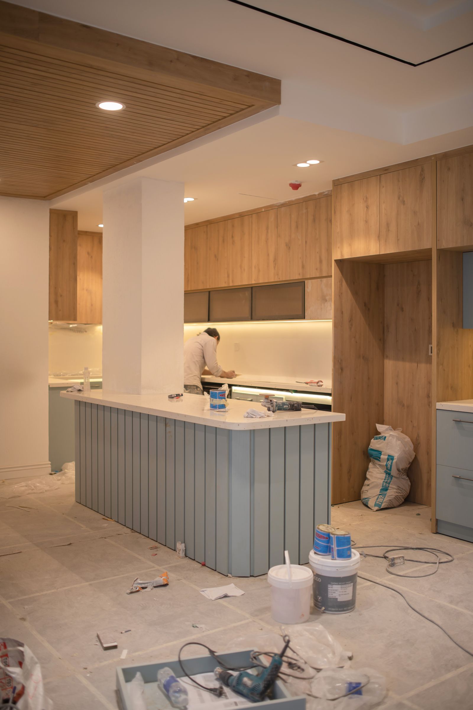 A kitchen nearing completion, cabinetry installed and a worker finishing the island.
