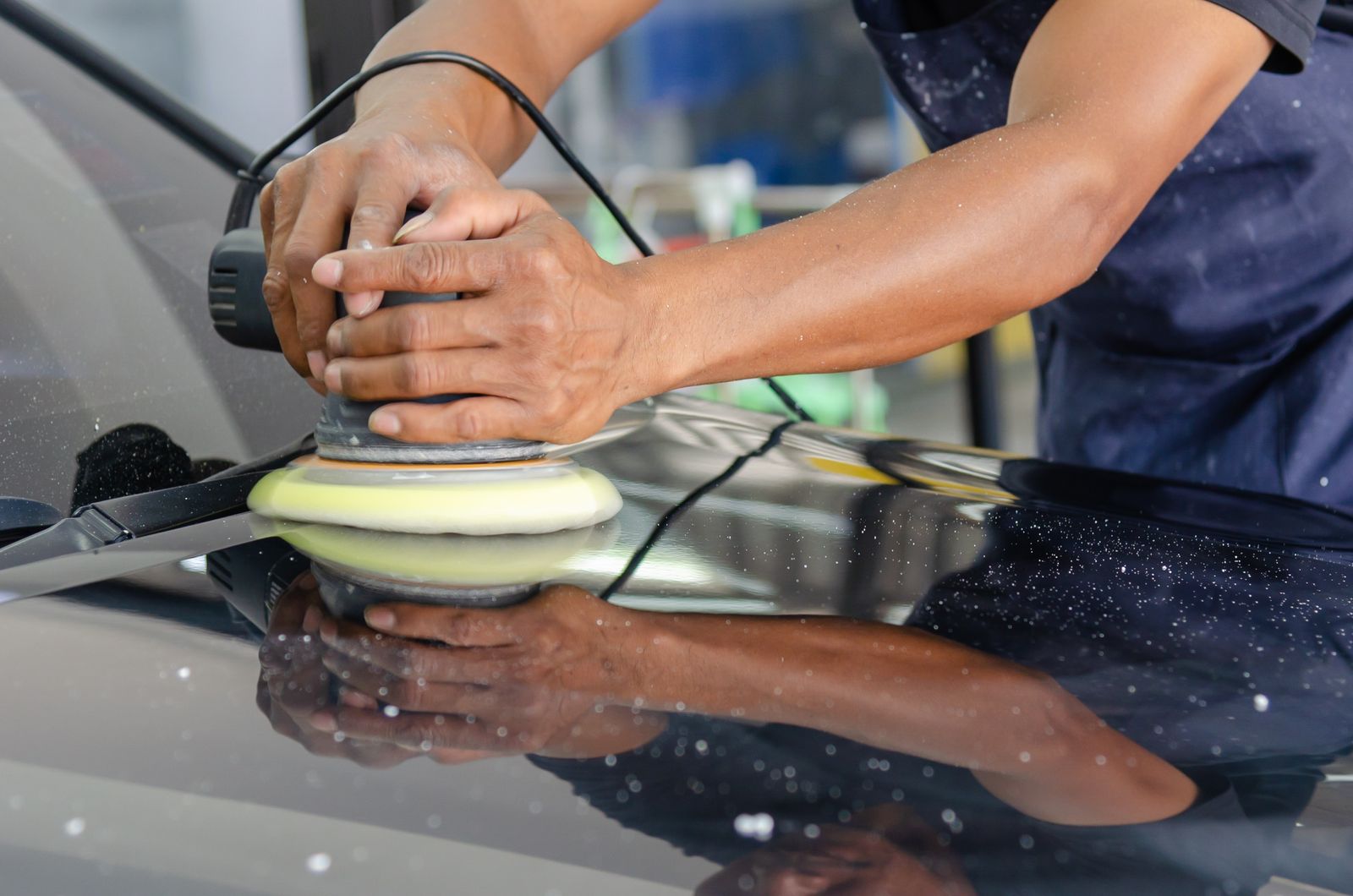 Hands guiding a polishing machine over a dark vehicle panel