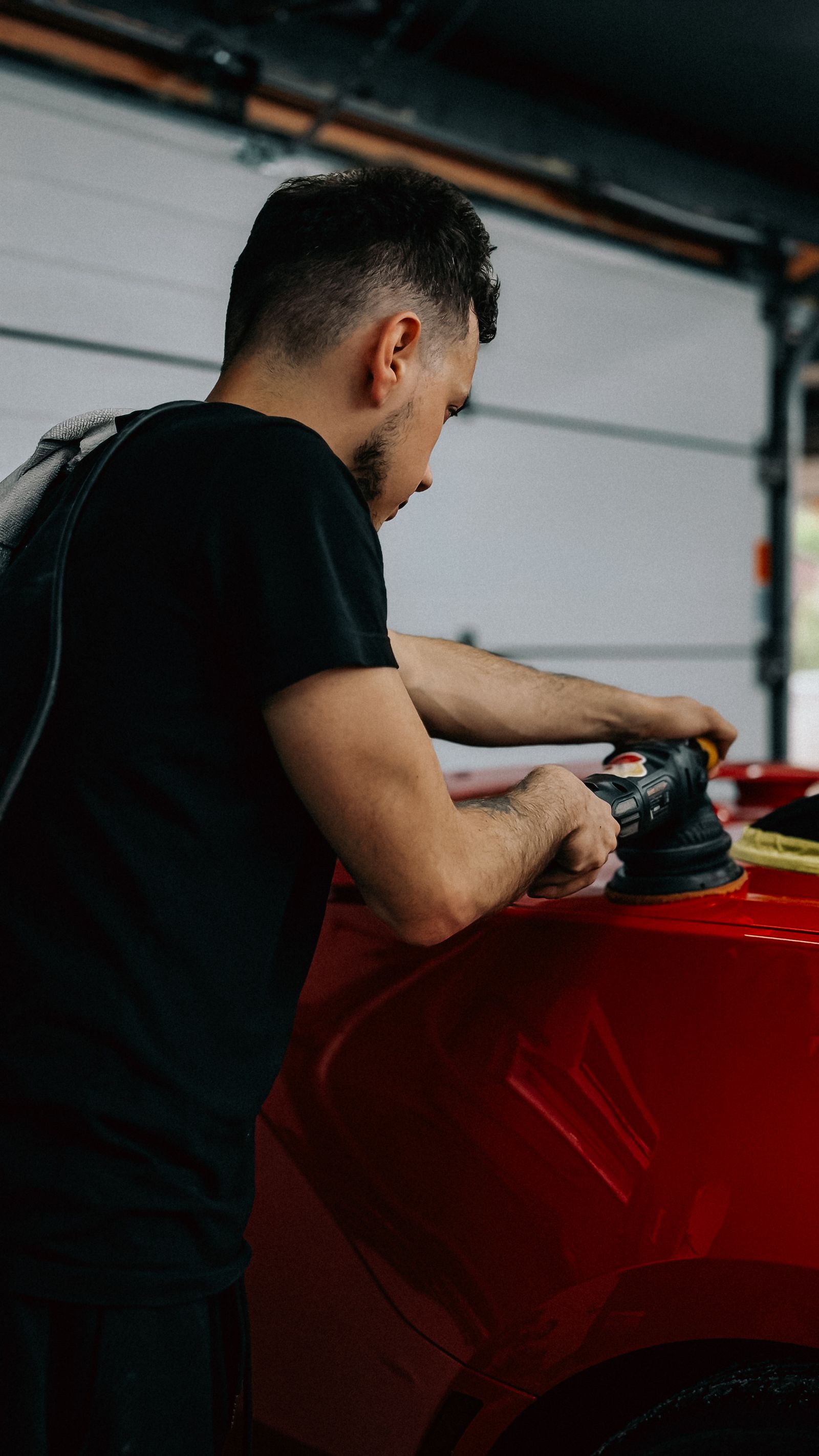 A technician using a polishing tool on a red car