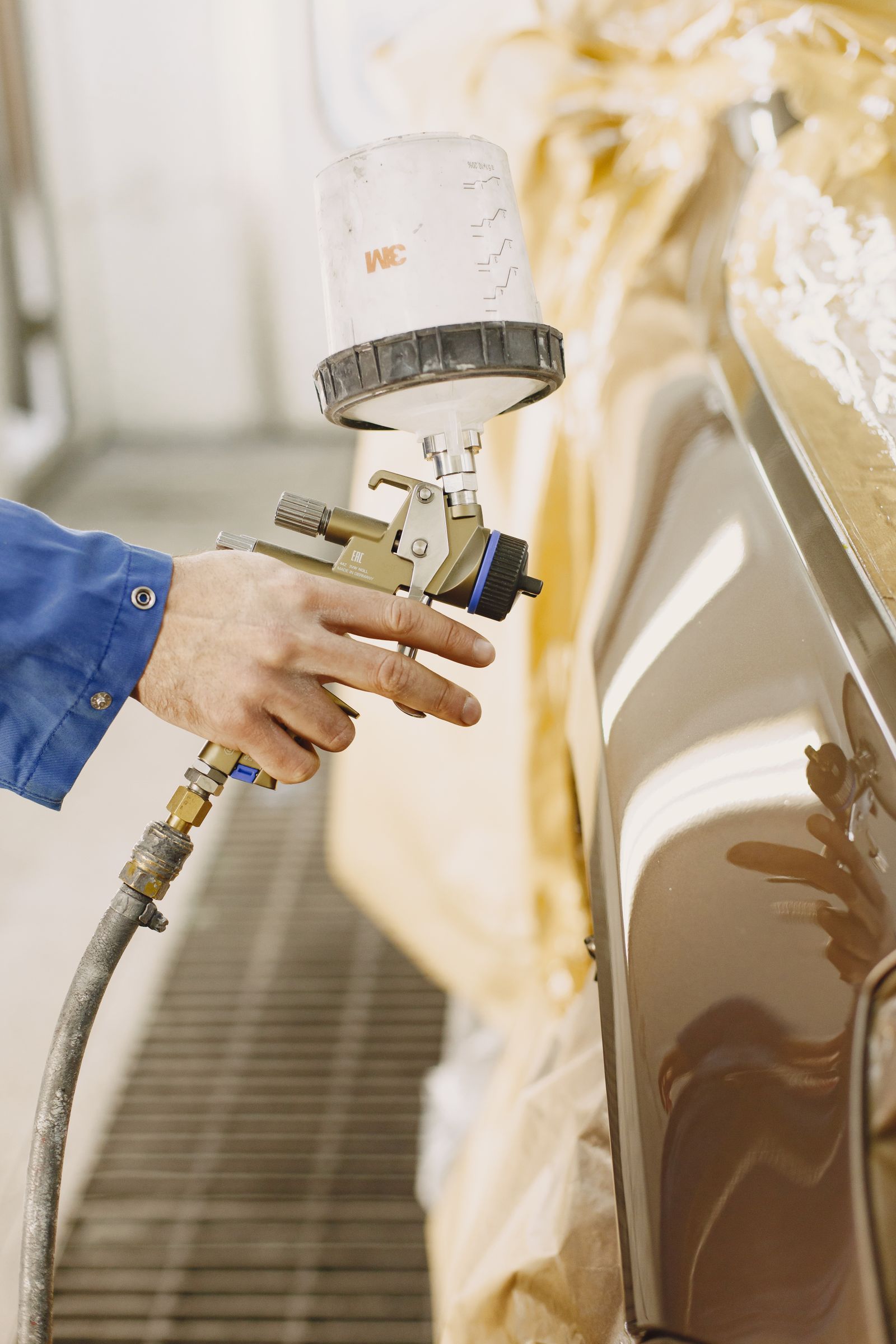 A hand holding a spray gun near a vehicle panel