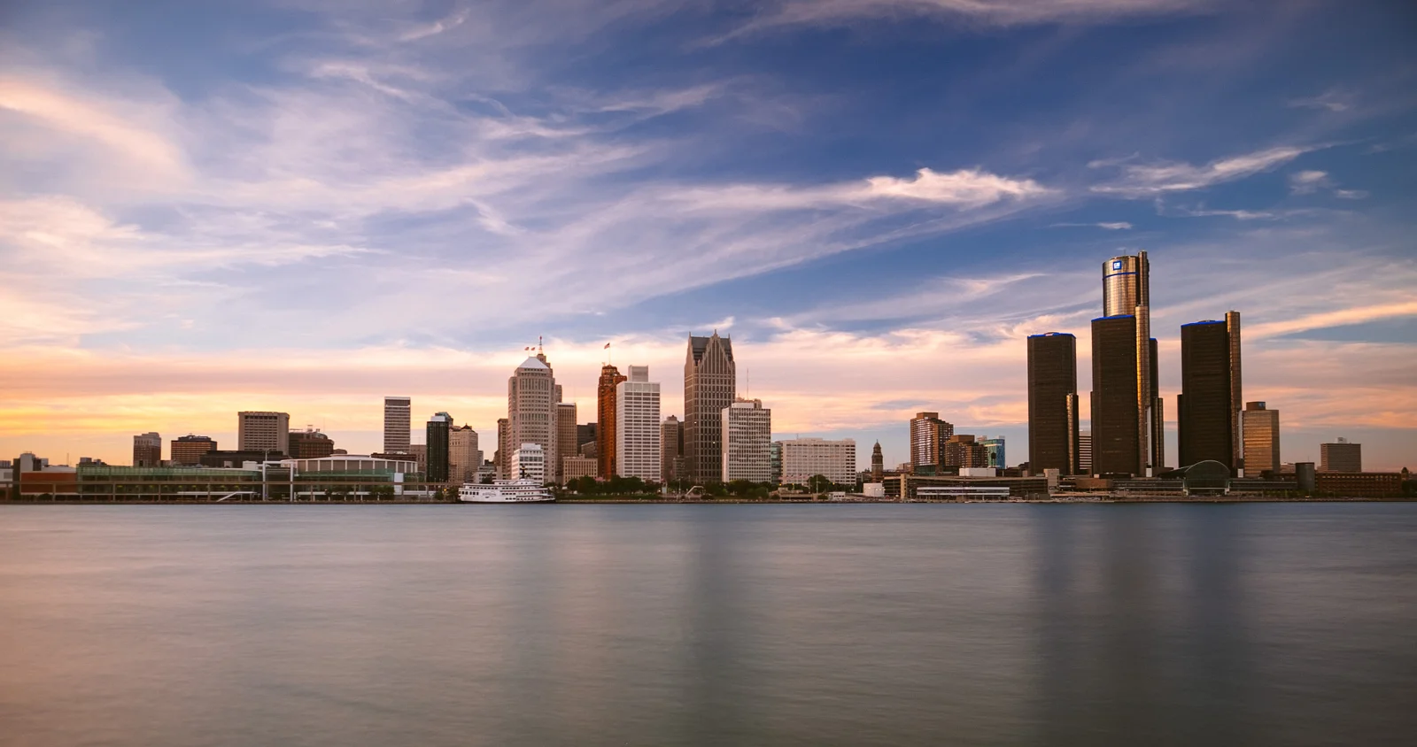 Detroit’s skyline across the river under a pink and violet evening sky.