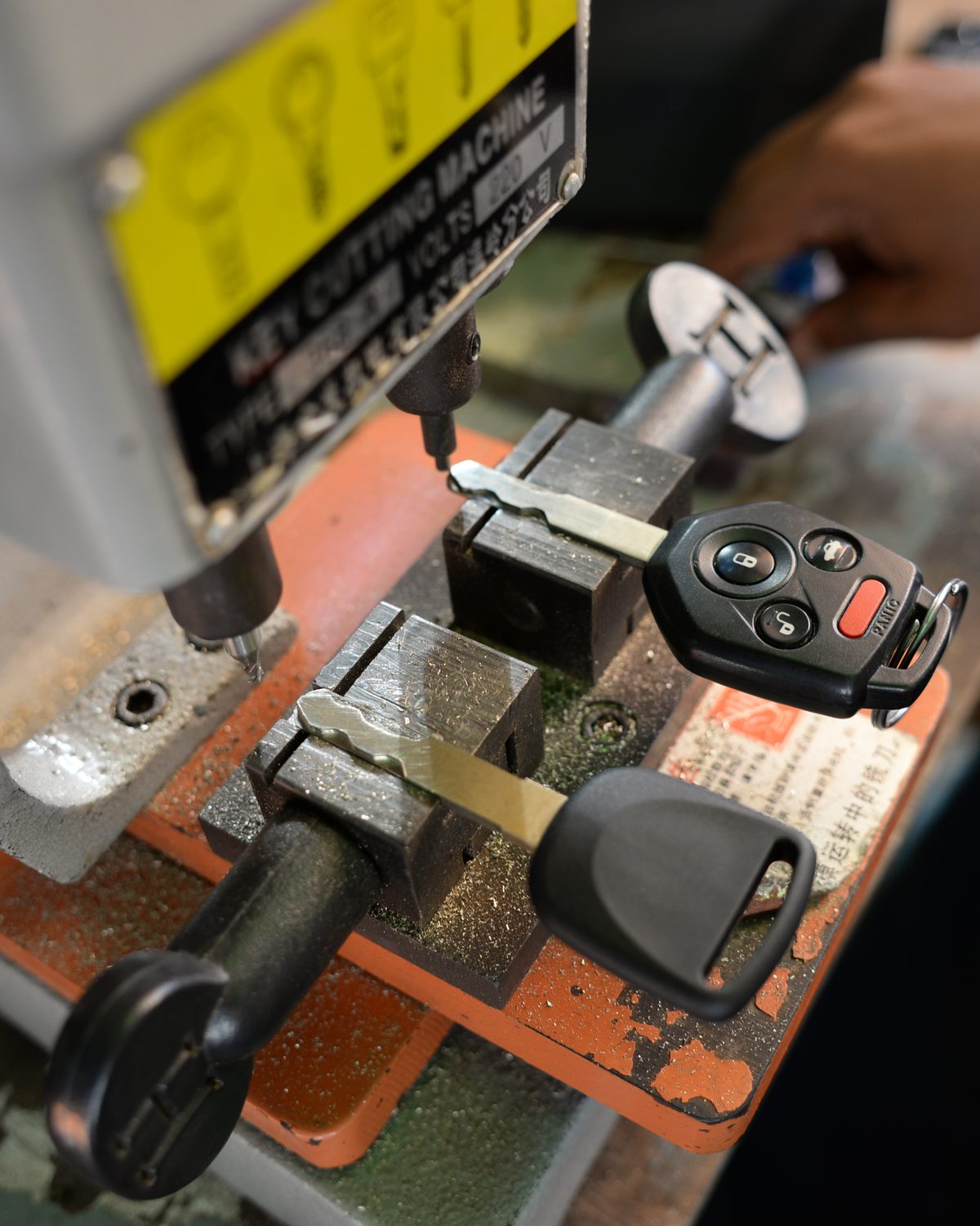 A locksmith's hands cutting a car key on a bench-mounted duplicating machine.