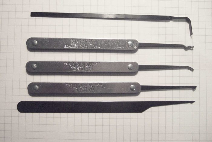 Four lock picks and a tension wrench laid out on graph paper, part numbers legible along the shafts.