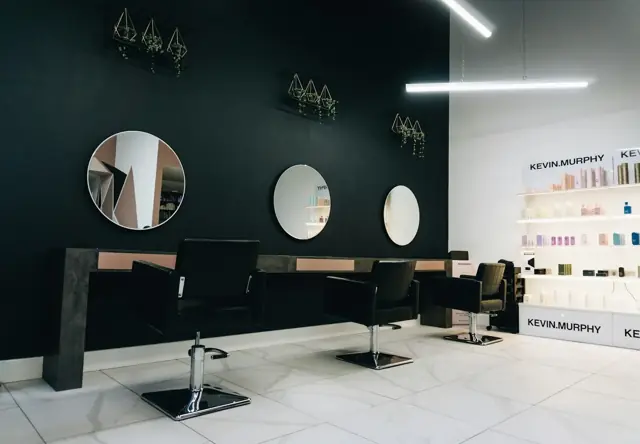 A row of styling chairs facing round mirrors on a black wall