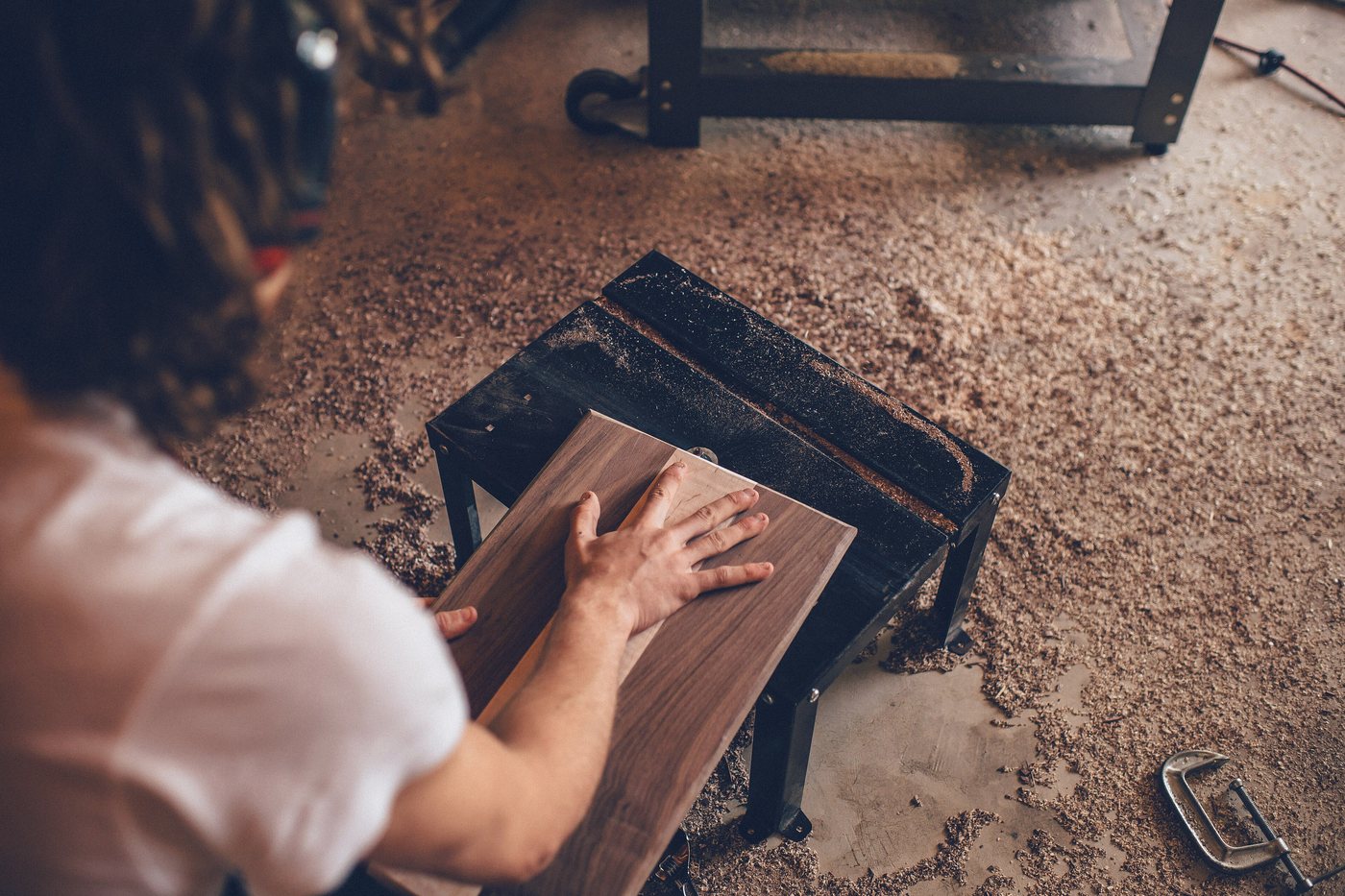 Someone working a board flat on a bench, both hands on the tool, the floor under them covered in shavings