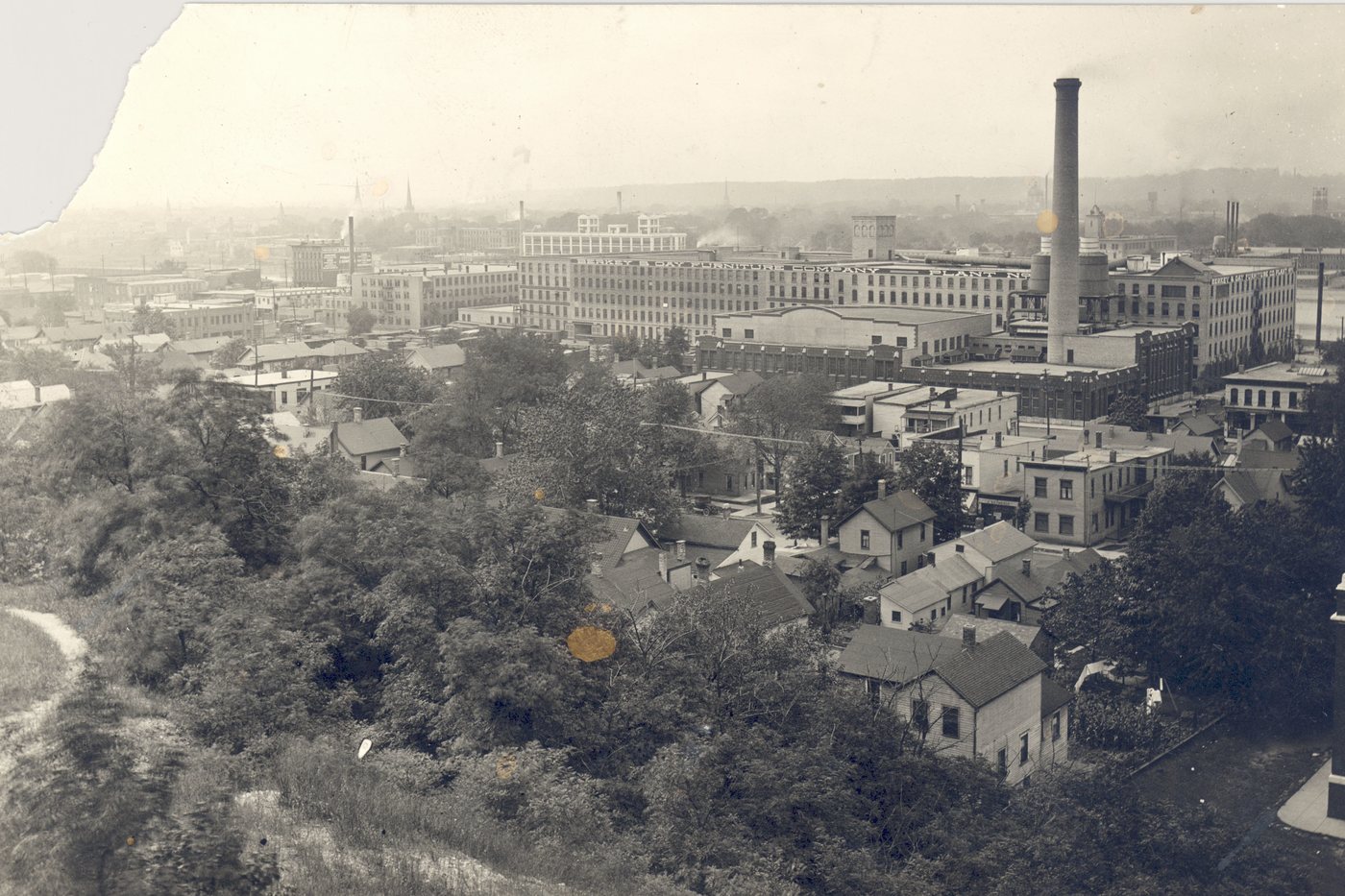 The Berkey and Gay furniture works seen from above in 1924 — a dense block of multi-story brick factory buildings and a tall chimney, with the houses of Grand Rapids running away below it