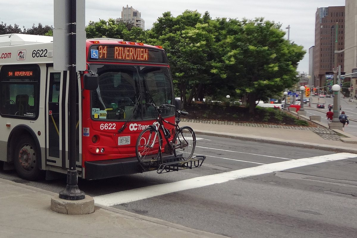 A city bus at a curb with a loaded bicycle rack folded down across its front bumper