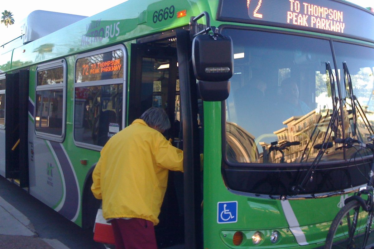 A passenger stepping onto a city bus through the front door, the international symbol of access displayed beside the doorway