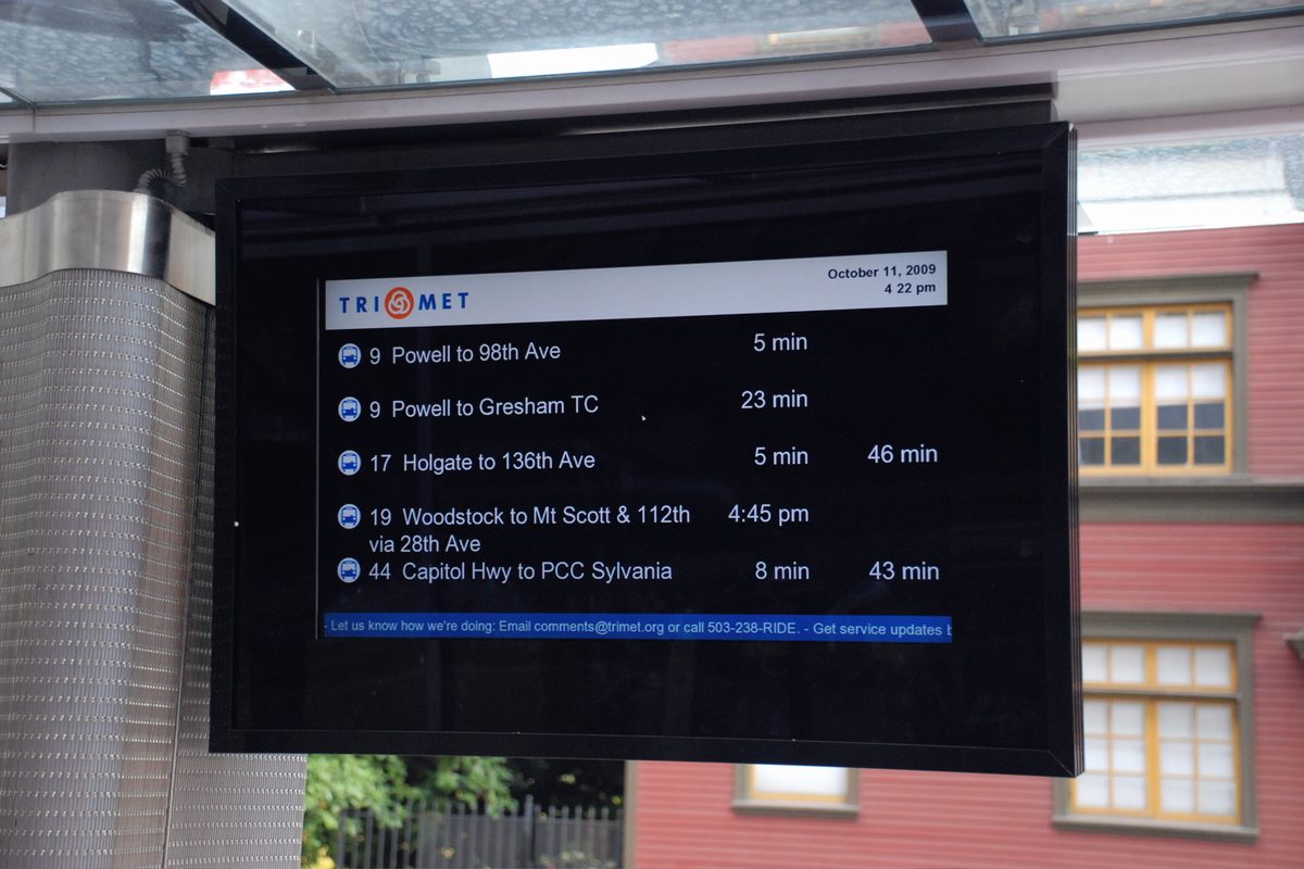 An electronic arrival display at a transit stop listing route numbers, destinations and minutes until arrival