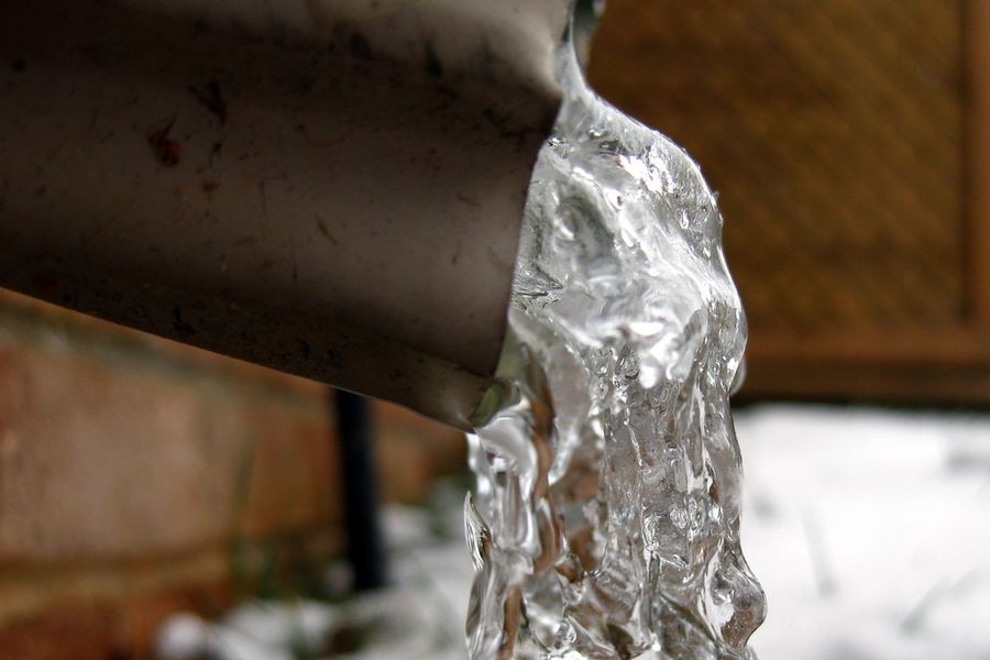 Water pouring from a split pipe in freezing weather, ice already forming on the ground below it.