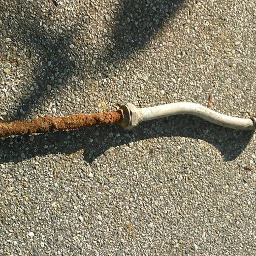 A lead gooseneck cut out of a water service line, lying on the road surface.