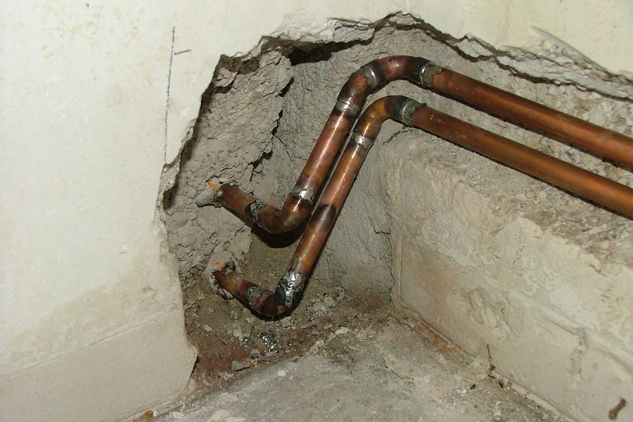 Copper supply pipes bent around a corner inside an opened plaster wall.