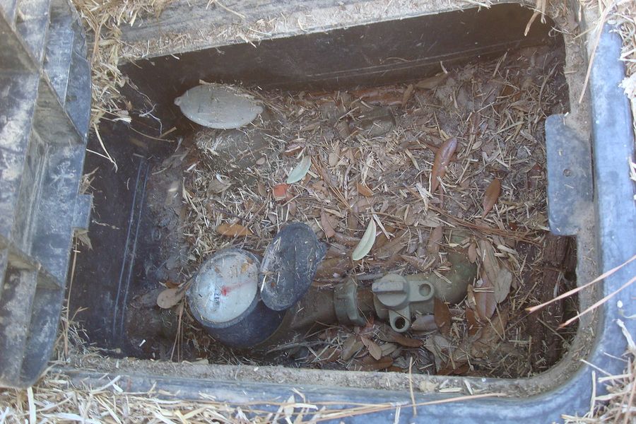 A household water main and meter in a crawlspace, wrapped and half buried in loose insulation.