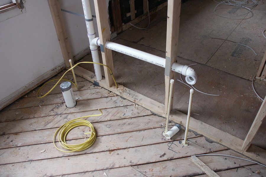 Plastic drain and vent piping roughed in through the framing of a gutted bathroom.