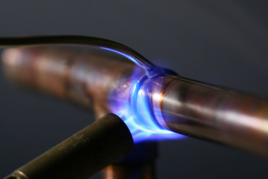 A propane torch flame playing on a copper pipe joint while it is soldered.