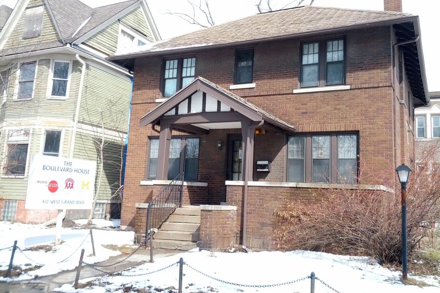 A two-story brick house with a covered porch on a Southwest Detroit street in winter.